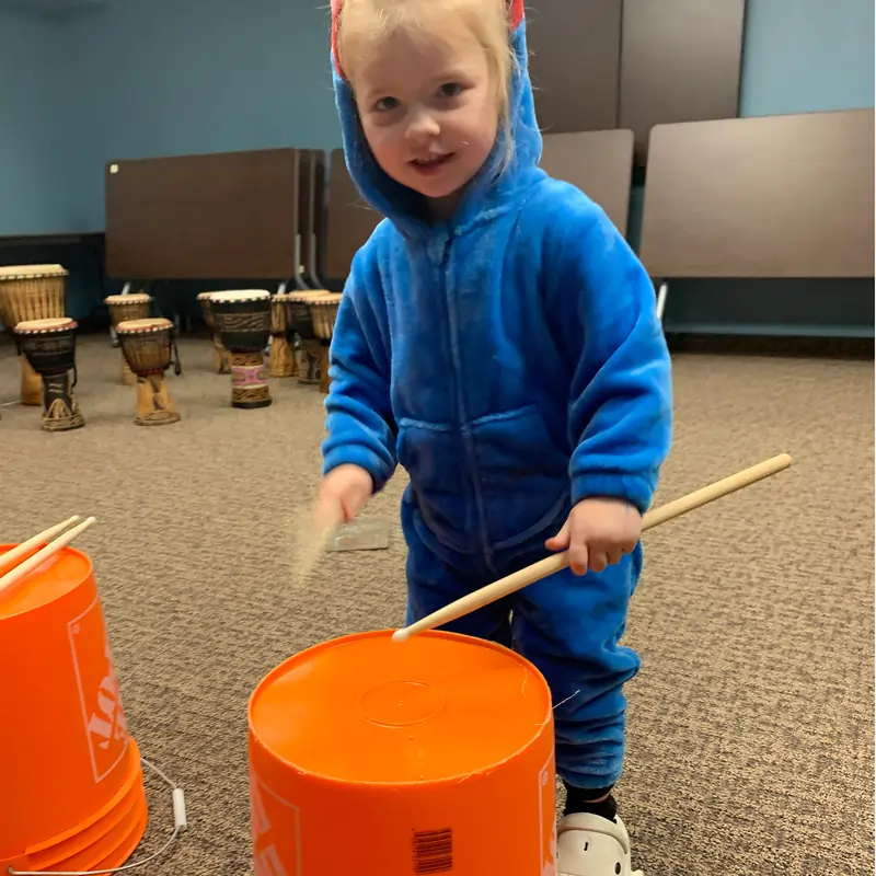 a small girl in a costume for halloween playing drums